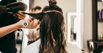 “Hairstylist using a round brush and blow dryer to style a client’s hair in a well-lit salon.”