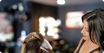 “Hairstylist applying highlights to a client’s hair in a modern salon, with soft lighting and a professional atmosphere in the background.”